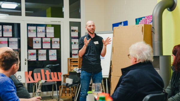 Mann steht vor Flipchart in Raum und erklärt