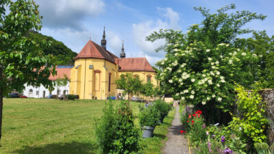 Fotografie eines Klostergartens, im Hintergrund ist die Klosterkirche zu sehen