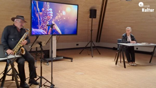 Eine Mann mit Saxophon und eine Frau mit Buch an einem Tisch