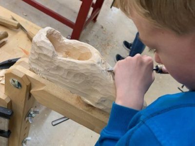 Kind bearbeitet mit einem Stechbeitel einen Holzschuh