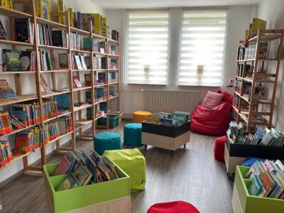 Kinderbereich der Bibliothek mit Bücherregalen, Sitzhockern und Bücherkisten