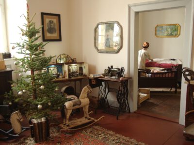 Historischer Wohnraum mit Weihnachtsbaum, Schaukelpferd, Nähmaschine und Blick in ein historisches Schlafzimmer