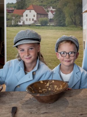 Zwei Kinder in historischer Müllerkluft vor einem Tisch mit Schüssel.