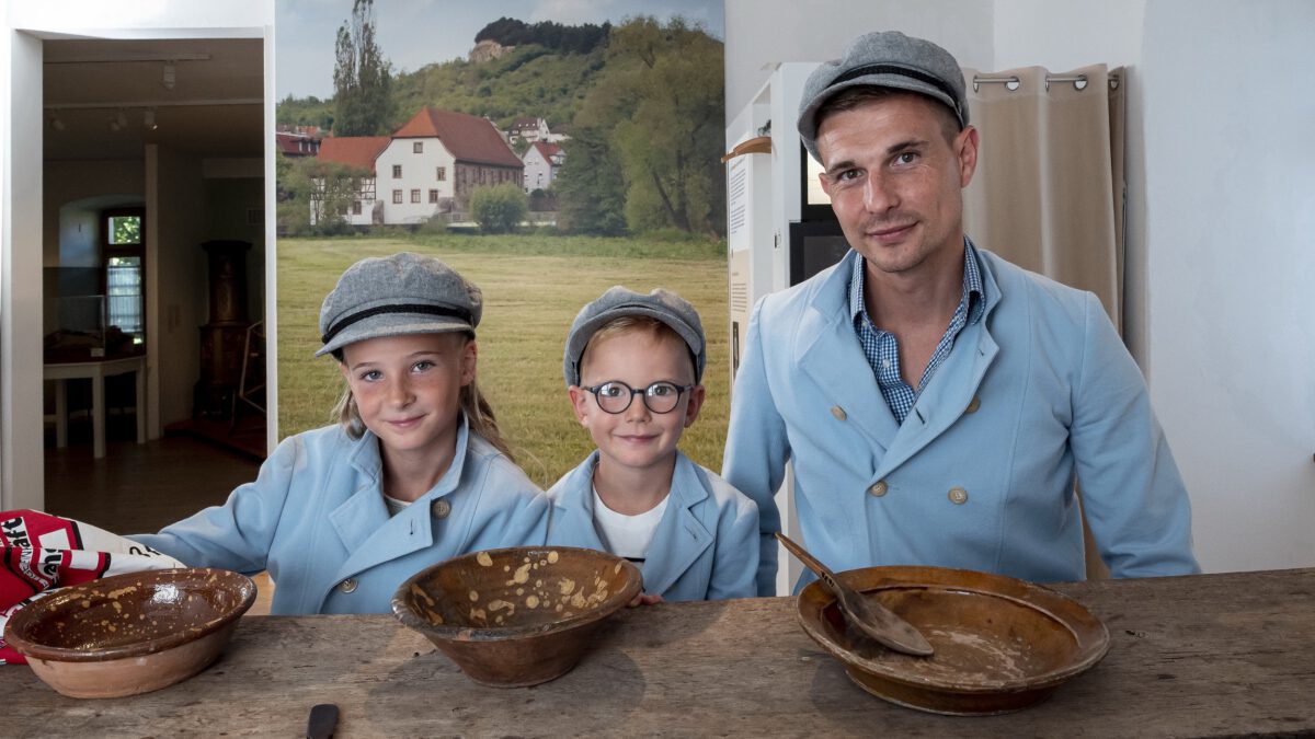 Mann und zwei Kinder in historischer Müllerkluft vor einem Tisch mit Schüsseln.