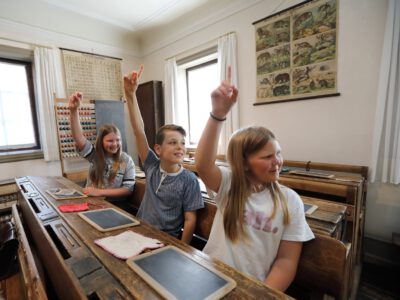 Drei Kinder melden sich bei einer historischen Unterrichsstunde im Museum.