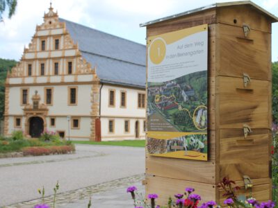 Startpunkt Bienenlehrpfad mit Infotafel und Gebäude im Hintergrund