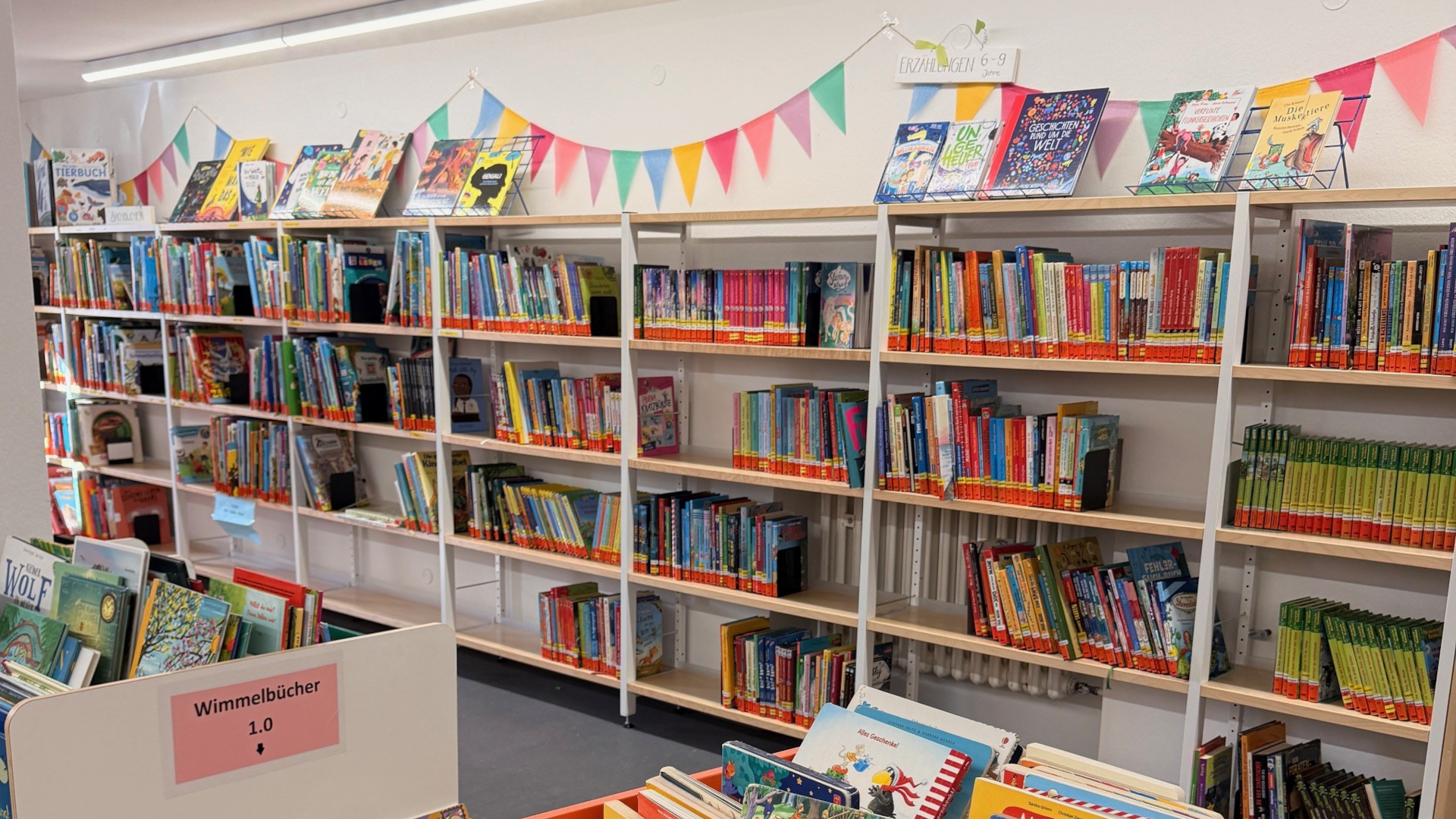 Büchertisch und Bücherregale mit Kinderbüchern; Wimpelkette an der Wand