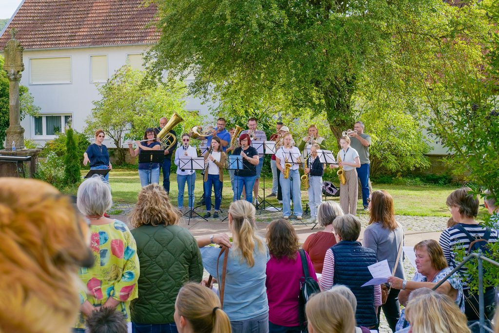Personen mit Instrumenten musizieren vor stehenden Zuschauern und Zuhörern
